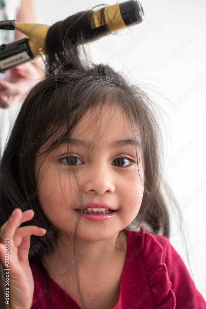 Fototapeta premium Stylist curling hair for little girl in a parlor