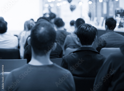 Speaker giving a talk at a corporate business conference. Audience in hall with presenter in front of presentation screen. Corporate executive giving speech during business and entrepreneur seminar. 