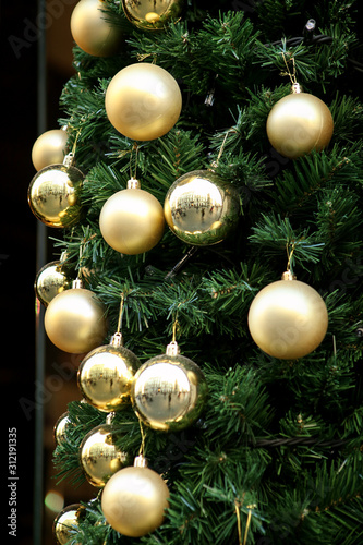 Traditional decorated Christmas baubles on wreath made of green fir or spruce branches and glowing garland outdoors. Twigs pine, gold and silver Christmas balls as decorations for New Year holidays.