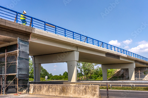 Obraz na plátne Worker mount renewing blue fence on overpass over highway