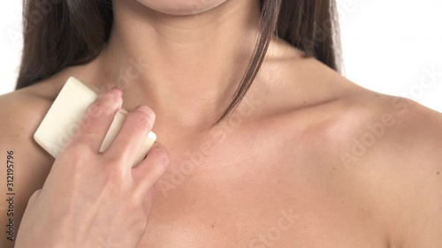 Close-up shot of a naked female shoulders. Woman is gently touching her decollate with a bar of soap. Spa and wellness concept