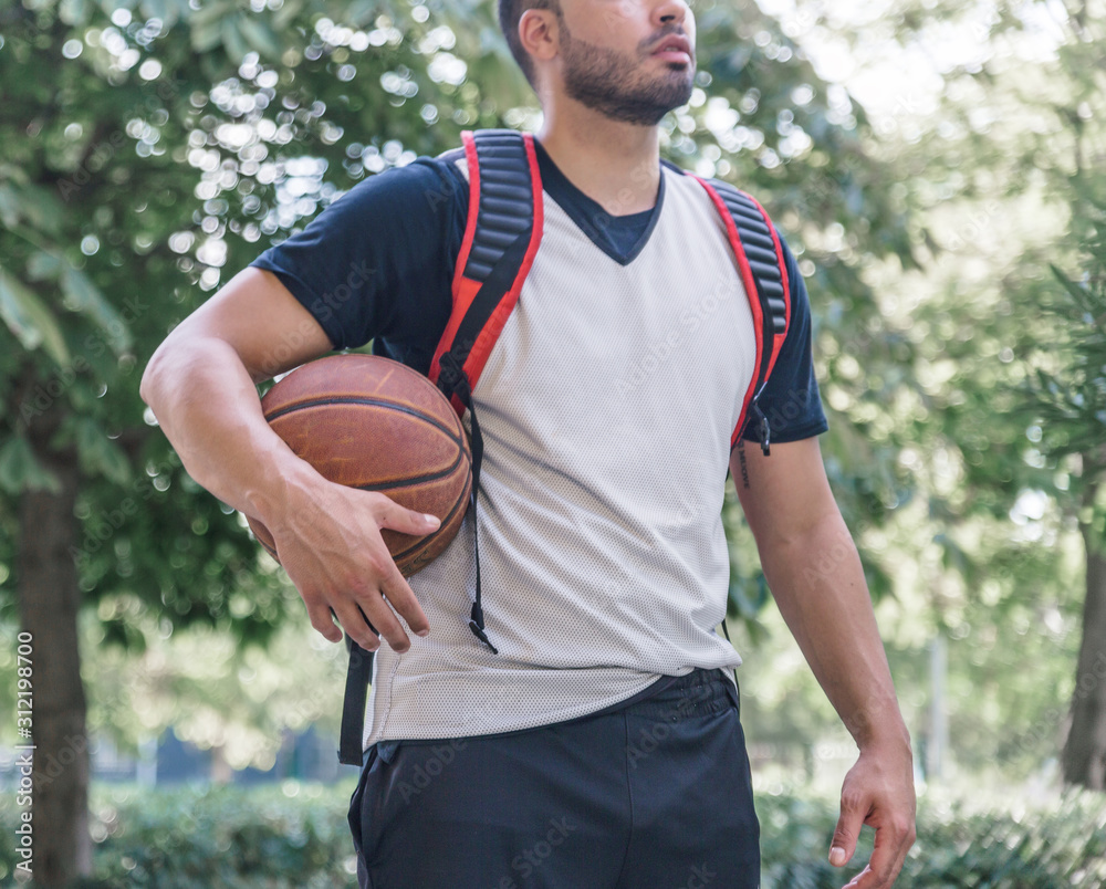 Forefront of an athlete basketball player with his orange ball and a backpack behind his back