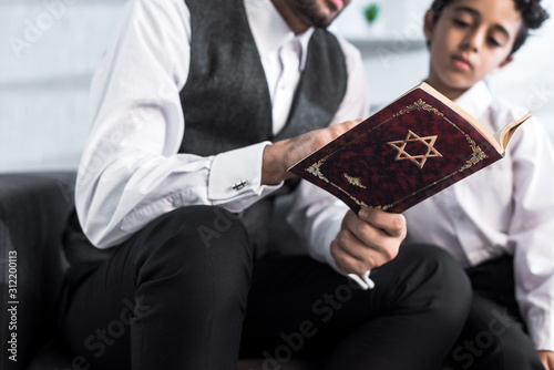 Fotografie cropped view of jewish father and son reading tanakh in apartment