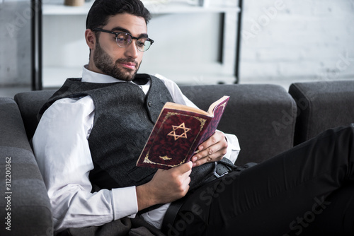 handsome and young jewish man in glasses reading tanakh
