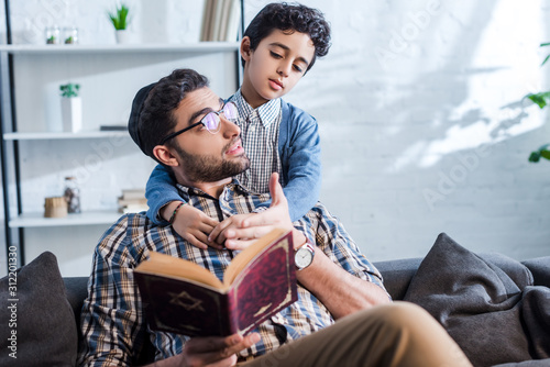 jewish father holding tanakh and talking with son in apartment photo