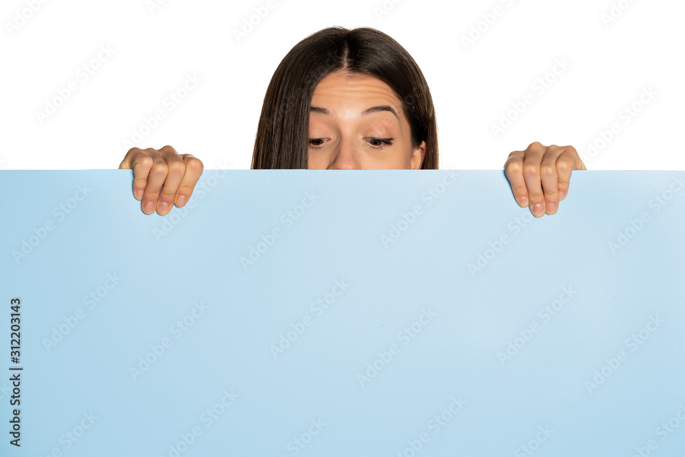 young beautiful woman peeking behind a blue empty board on white background young beautiful woman peeking behind a blue empty board on white background