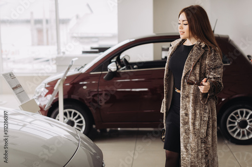 A stylish young girl is choosing  a new car in a car store © dsheremeta