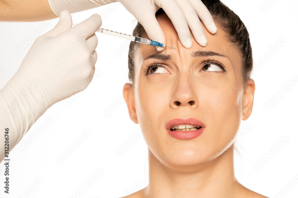 Portrait of a young scared woman on a faace filler injection procedure on white background