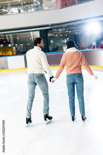 rear view of young couple holding hands and skating on rink