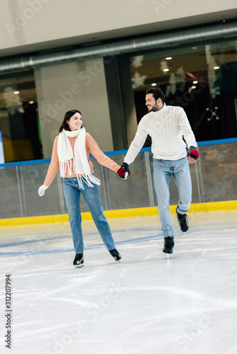 young couple holding hands and skating on rink