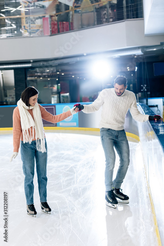 cheerful young woman teaching man to skate on a rink