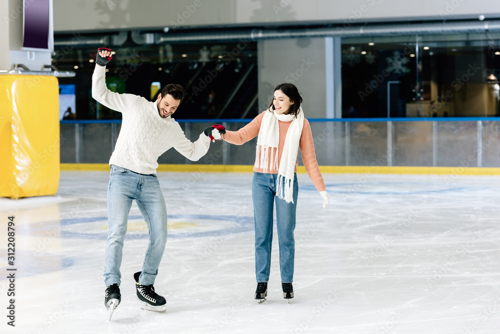 happy woman teaching smiling man to skate on a rink and holding hands