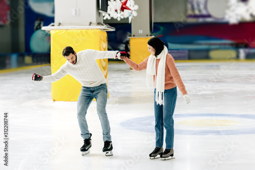 beautiful young woman teaching man to skate on a rink and holding hands