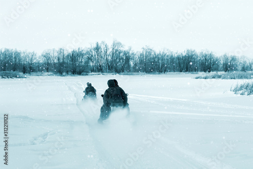 Billede på lærred Men on two snowmobiles go on the winter river. View from the back