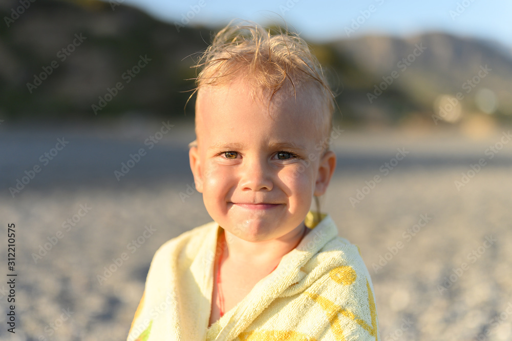 dreamy three year old little boy resting on the sea beach after swimming during the Golden hour