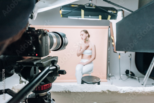 Selective focus of videographer with camera and model in photo studio with spotlights