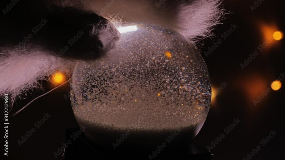 Christmas snow globe animation on hand. A garland of lights glows in the background.