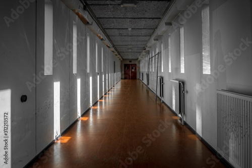 A long bare corridor with light and dark shadow spots. The corridor evokes an unpleasant and anxious feeling