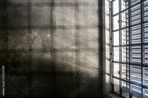 The very sober interior of a prison cell: barred windows with little light coming in and bare concrete walls