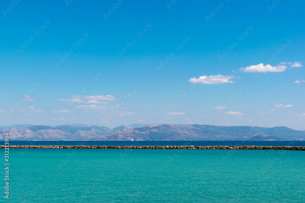 Colorful seascape. The bicolor sea is aquamarine and classic blue, the coastline of mainland Greece and the bright blue sky. Lefkimmi Port, Ionian Islands, Corfu, Greece. Space for text, quotes.
