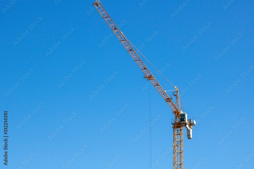 Yellow colored tower crane is being used in construction to lift cargo. Yellow colored tower crane is being used in construction to lift cargo.