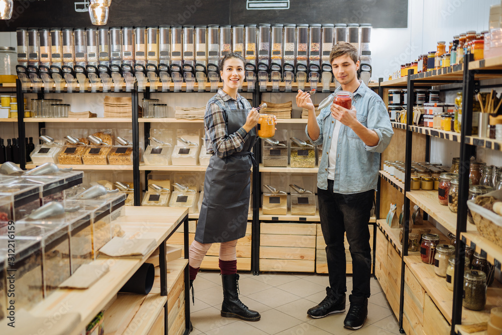 Obraz premium choosing in grocery shop. Zero waste shopping - man buying healthy food in bulk products in dispensers and food available. Sustainable shopping at small local businesses.