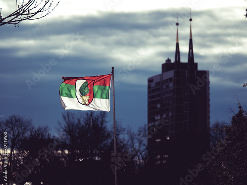 Augsburg, Germany - December 15, 2019: Illuminated flag of the soccer club FC Augsburg flatters in the wind with stormy dark clouds and the cityscape of Augsburg in the background photo