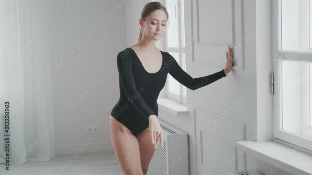 girl in a black bodysuit is warming up in a bright studio. dancer doing stretching sitting on the floor girl in a black bodysuit is warming up in a bright studio. dancer doing stretching sitting on the floor