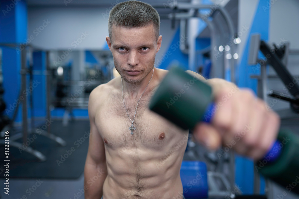 Muscular guy with nude torso trains in gym