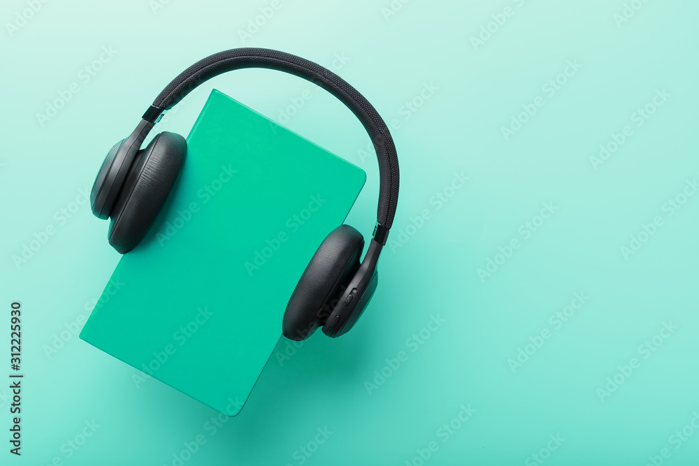 Headphones are worn on a book in a blue hardcover on a blue background, top view. Headphones are worn on a book in a blue hardcover on a blue background, top view.