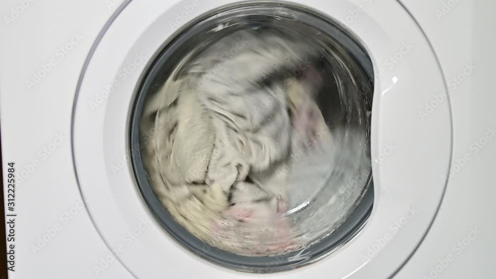 Washing machine door with rotating garments inside. focus in the center of dirty laundry and washing machine on the frame	