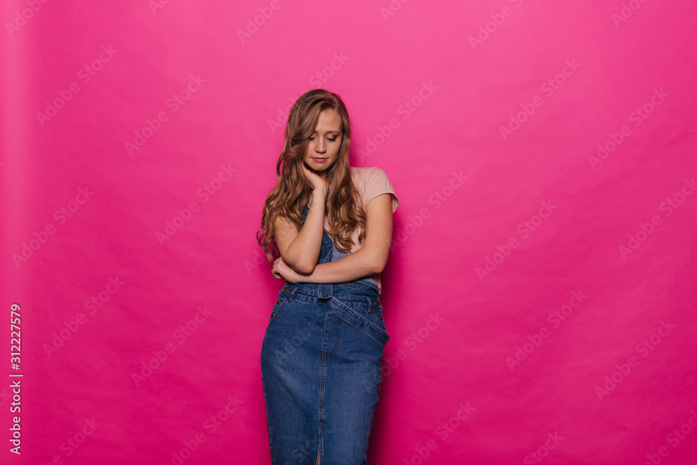 Beautiful serious young woman is thinking and thoughtful on isolated pink background. Charismatic girl is showing concept of emotions in professional studio.