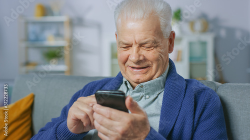Portrait of Progressive Senior Man Sitting in His Living Room Easily Uses Smartphone, Does Touching Gestures and Feels Very Comfortable with New Technologies.