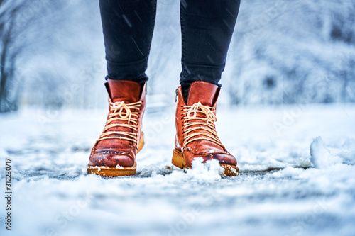 Feet of a woman on a snowy sidewalk in brown boots. Winter slippery pawement. Seasonal weather concept