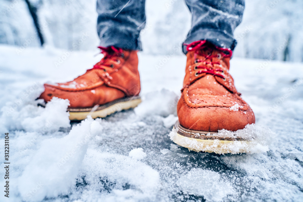 Feet of a man on a snowy sidewalk in brown boots. Winter slippery pawement. Seasonal weather concept Feet of a man on a snowy sidewalk in brown boots. Winter slippery pawement. Seasonal weather concept