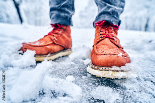 Feet of a man on a snowy sidewalk in brown boots. Winter slippery pawement. Seasonal weather concept photo