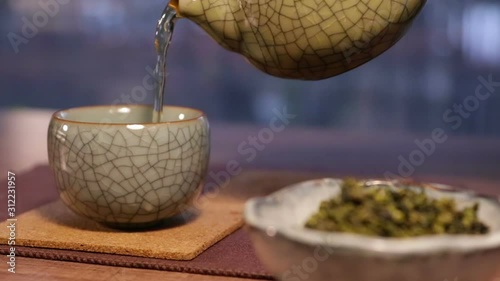 Pouring a Tea Cup, See a Bowl of Oolong Leaves in a Foreground (ID: 312231957)