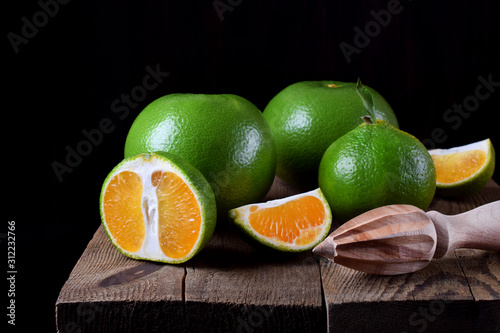 Green mandarins cut in halves and segments and whole sweetie on the wooden table