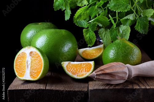 Green mandarins cut in halves and segments and whole sweetie on the wooden table