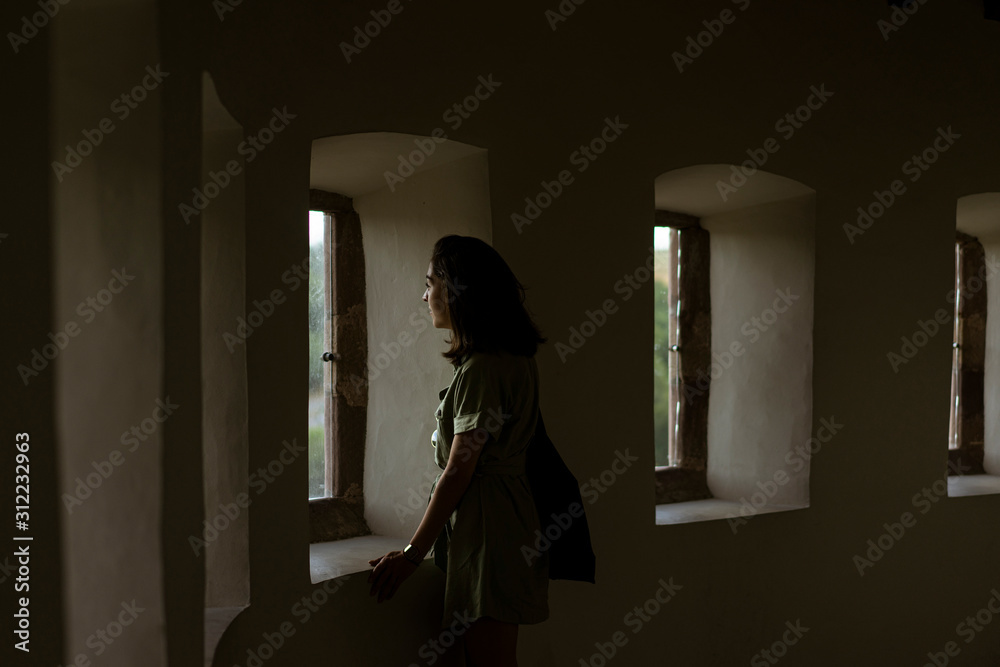 Young woman at home looks through the window to the outside