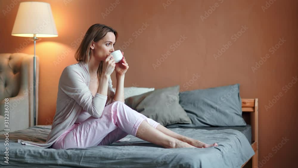 Happy relaxed barefoot young woman drinking hot tea in bedroom enjoying weekend at home Happy relaxed barefoot young woman drinking hot tea in bedroom enjoying weekend at home