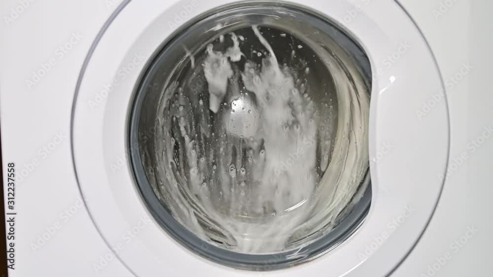 Washing machine door with rotating garments inside. focus in the center of dirty laundry and washing machine on the frame	