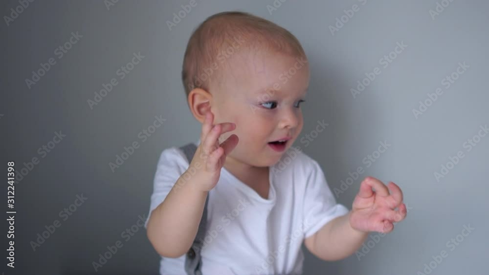 The boy claps his hands, children's emotions, a happy childhood, the adaptation of the child in kindergarten. Portrait of the two-year blue-eyed boy in a white T-shirt The boy claps his hands, children's emotions, a happy childhood, the adaptation of the child in kindergarten. Portrait of the two-year blue-eyed boy in a white T-shirt
