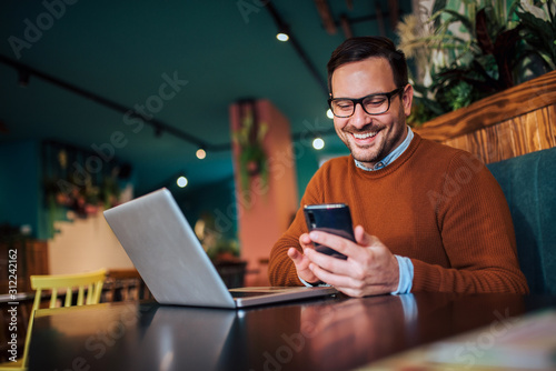 Portrait of a smiling man using smart phone and laptop in the cafe.