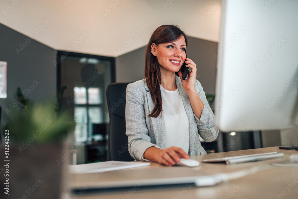 Beautiful businesswoman talking on mobile phone and using computer. Beautiful businesswoman talking on mobile phone and using computer.