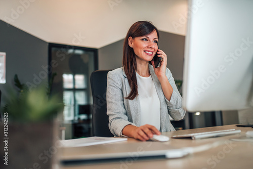 Beautiful businesswoman talking on mobile phone and using computer.