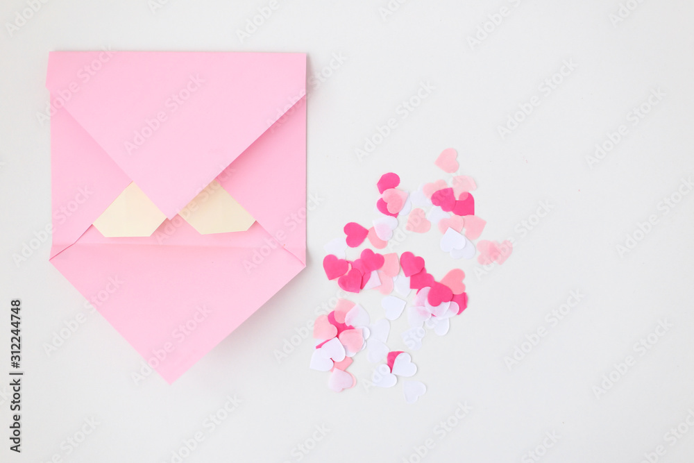 Flat lay: pink hand made envelope, confetti hearts, origami yellow heart made of paper for notes. Making postcard for Valentine's Day. Do it yourself. Photo from the series
