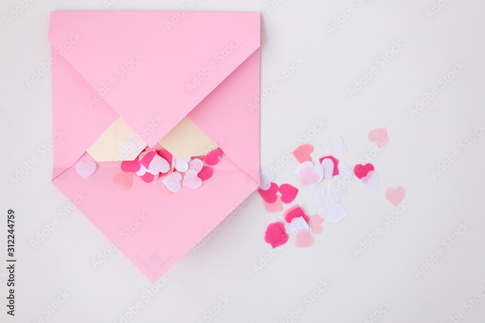 Flat lay: pink hand made envelope, confetti hearts, origami yellow heart made of paper for notes. Making postcard for Valentine's Day. Do it yourself. Photo from the series