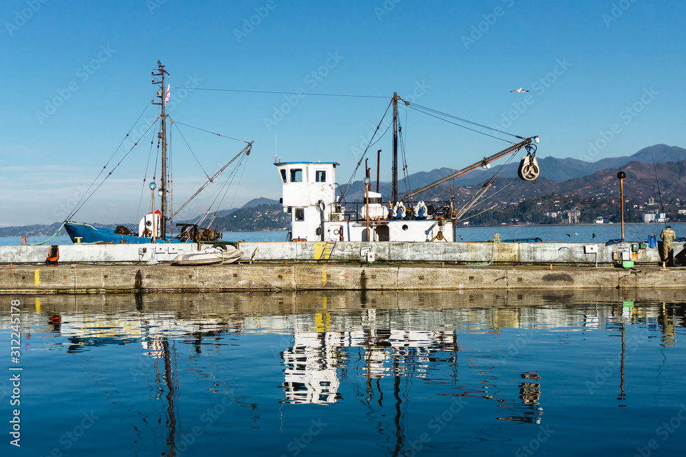 Fishing boat with a crane in a sea port. Sunny day blue sky with mountains in the background. Travel vibrant background.