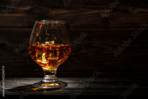 Whiskey with ice or brandy in a glass and a square carafe on an old wooden background. Whiskey with ice in a glass. Whiskey or cognac. Selective focus. © yuriivd